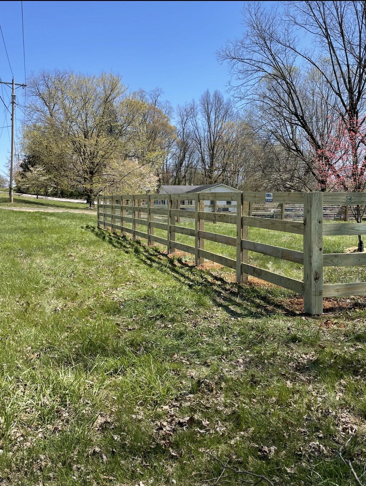 Four-board wooden farm fence with wire mesh running along a grassy yard